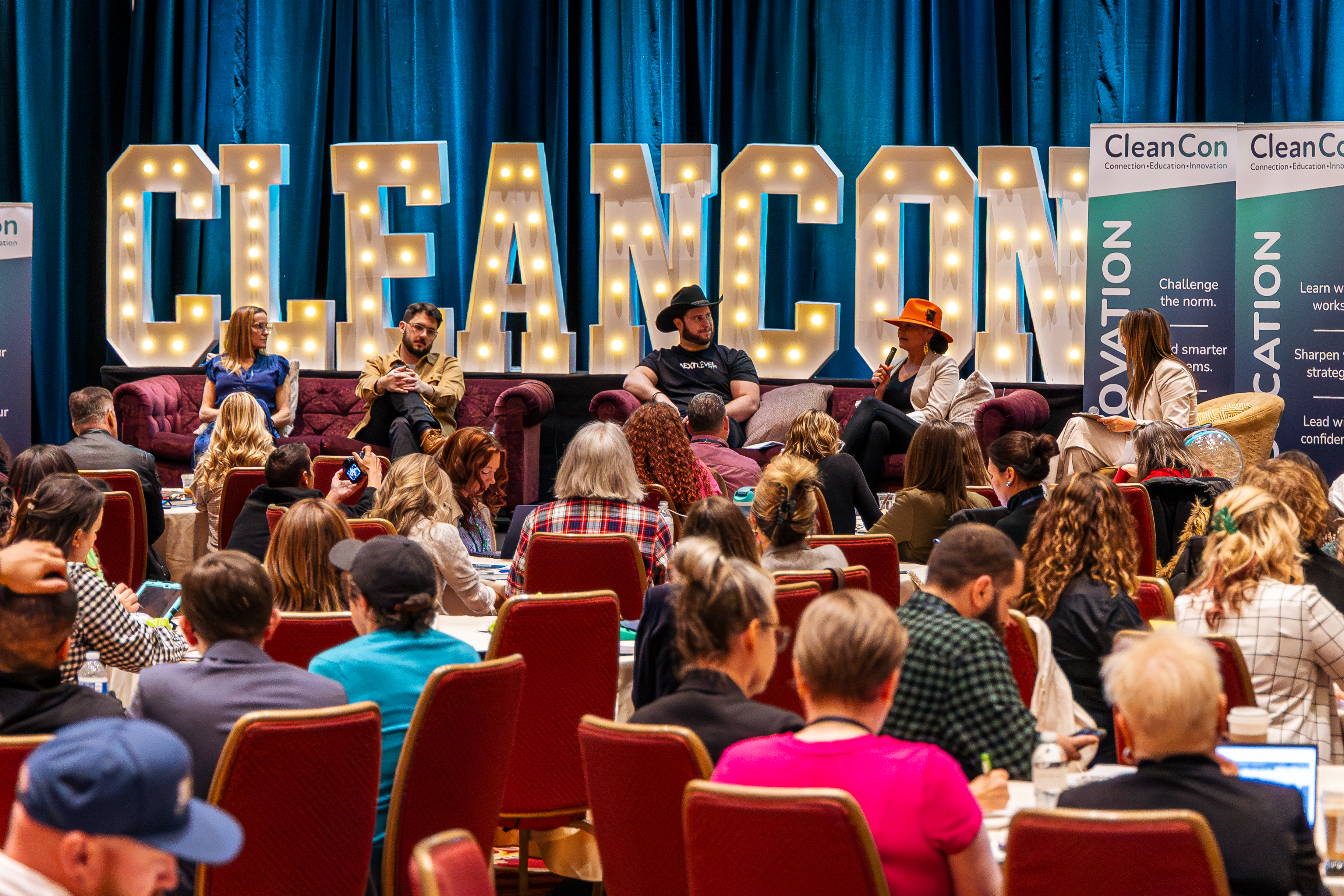 Attendees seated in front of illuminated CLEANCON marquee letters at a CleanCon event
